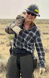 Female Firefighter, Jessica Race, carries a chainsaw over her right shoulder.