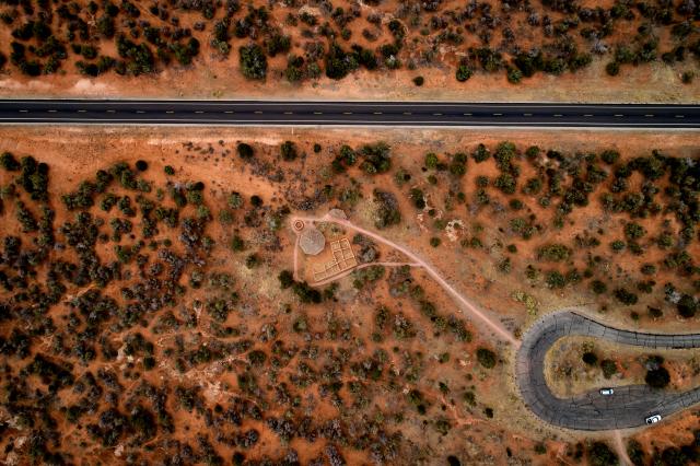 An aerial view of the Mule Canyon site with vehicles in the loop, the trail to the site and the close proximity to the road are shown. Vegetation is spread out on the landscape.