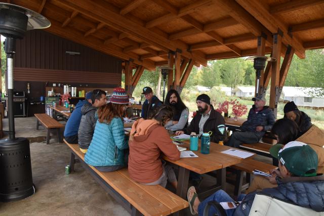 During a training with the Access Fund, BLM staff, and other partners, sit with the Climber Stewards in and outdoor pavilion and are speaking together.
