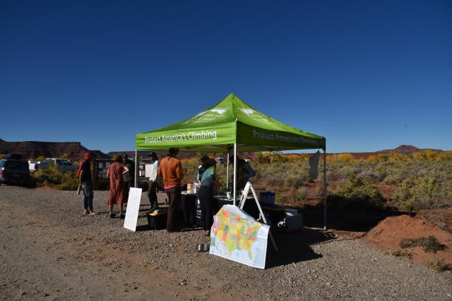 A tent with the words "protect America's Climbing" and individuals standing around a table talking.