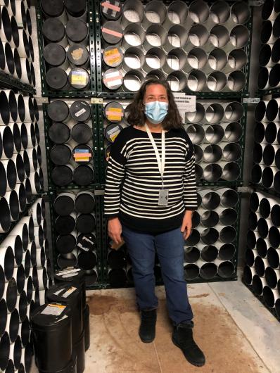 A woman standing in a room, the walls are lined with cylinders made to hold rolls of film.