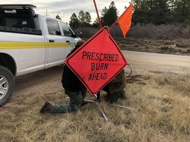 Two firefighters put up a sign that says prescribed burn ahead in front of a BLM truck in the Fall of 2021.