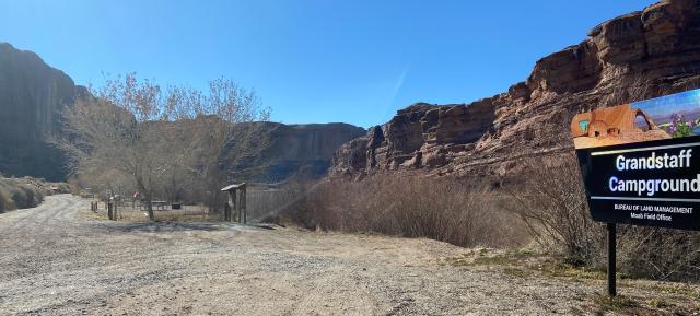 Bureau of Land Management signs with the agency branding reading Grandstaff Campground in front of a camping area and a tent. The river runs in the background.