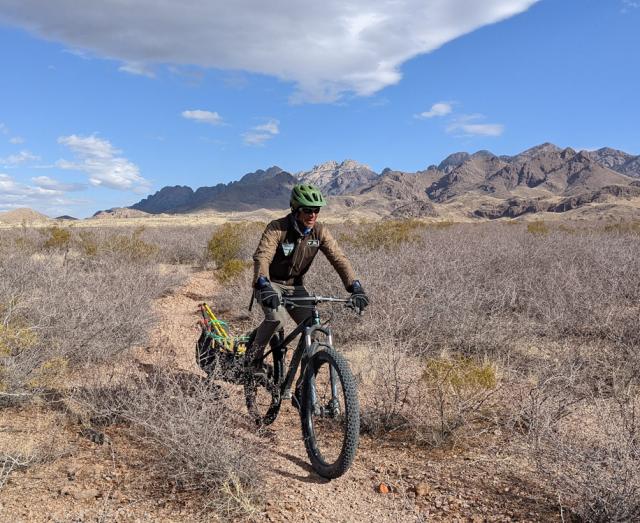 BLM park ranger rides mountain bike on a trail with mountains in background