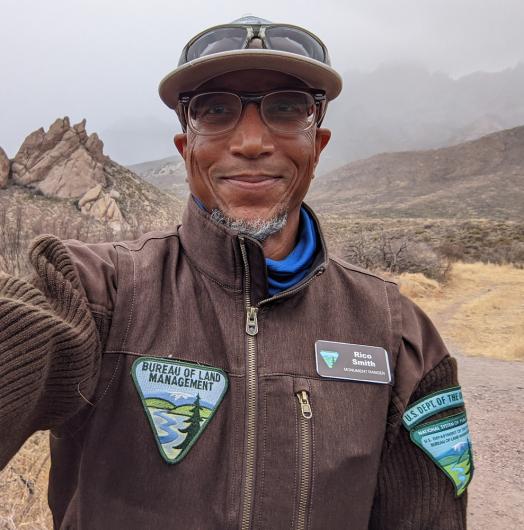 BLM park ranger poses on public lands with mountains in background