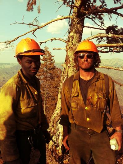 Two firefighter standing in front of a tree.