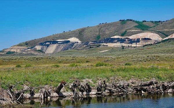 woody material on the banks of a stream. A phosphate mine is operating in the background.