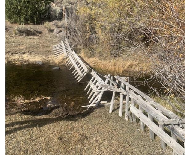 A broken gray fence strung across the stream