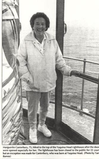 A grown up Marguerite at the top of the lighthouse as an adult. Her hand rests on the handrail and the lighthouse light is to her left.