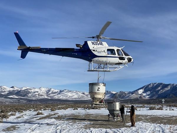 A helicopter dropping seed with two men on the ground. 