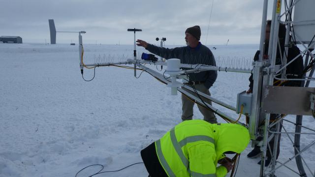 Scientists dressed in winter gear inspect the air quality monitoring equipment outside of the Kaktovik Air Quality Monitoring Station. 