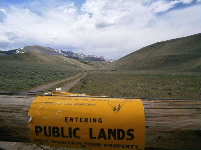 yellow sign wrapped around post "entering public lands". two track trail leading into the mountains