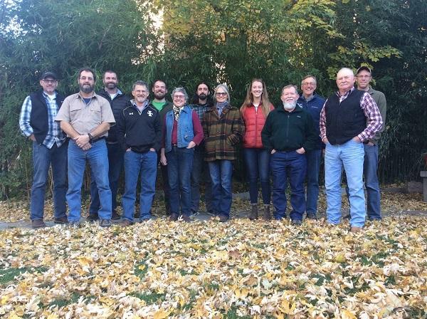 Partners in the study pose for a group photo. Leaves are on the ground and trees in the background. 