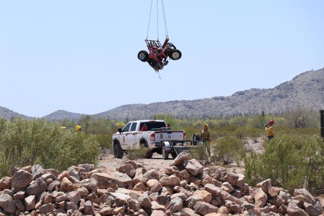 Helicopter in the air with a rope hanging from it. ATV is about to be dropped on to a trailer