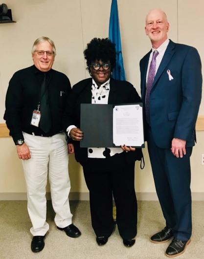 Woman stands with award, next to two men.