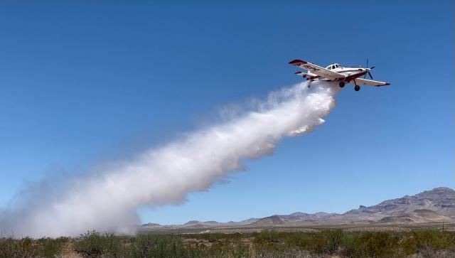 Single engine airtanker flying and dropping water on the landscape below