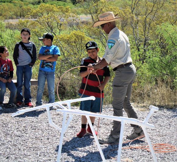 BLM Park Ranger Enrico Smith assists a Sunrise Elementary student with the rope lariat of the roping cattle experience.