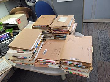 Stacks of files on top of a table in a cubicle.