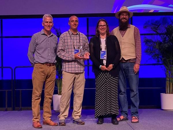 Group photo of NOC AIM Team standing on the stage and holding the award. 