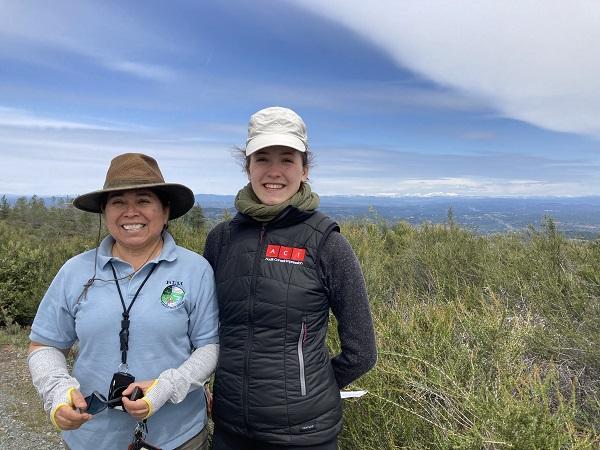BLM’s Pine Hill Preserve Manager Graciela Hinshaw stands with Margaux Blanc  at the Pine Hill Preserve. A field of brush is in the background. 