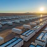 Bird's eye view of battery storage boxes with mountains and sun in the background. 