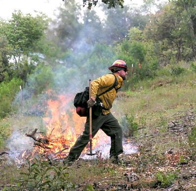 Person wearing hard hat and uniform tends a fire. 