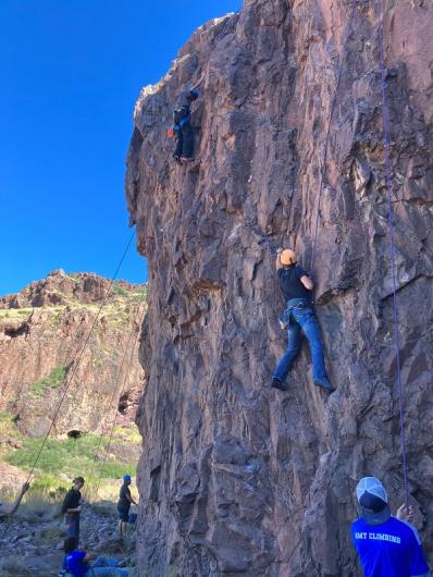 Two people climbing the rock face with four people on the ground below. 