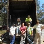 Six people stand behind a large storage truck with tires on the ground. 