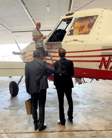 A SEAT pilot stands next to the window of his plane and is talking to two other men and giving them a run-through of his plane.