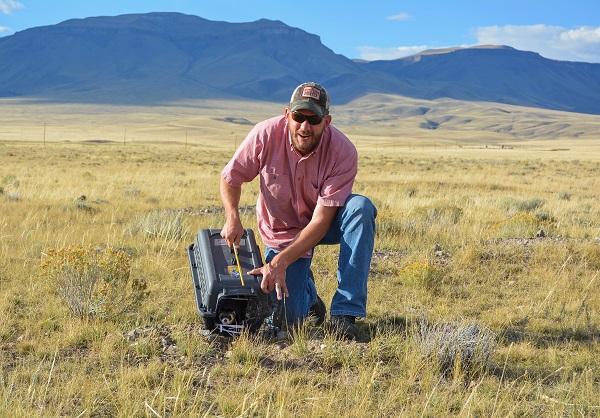 Cody Field Manager Cade Powell kneels down in the grass holding a cage with the ferret inside.