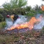 A person wearing a yellow uniform behind a small fire. 