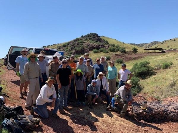 Large group of volunteers gathered for a photo. A truck and green hill are in the background. 