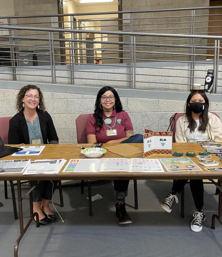 Three people sitting at a table with outreach materials