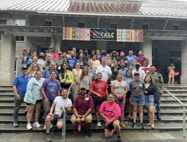 large group of people standing on the steps of a building with a NYCALC banner overhead