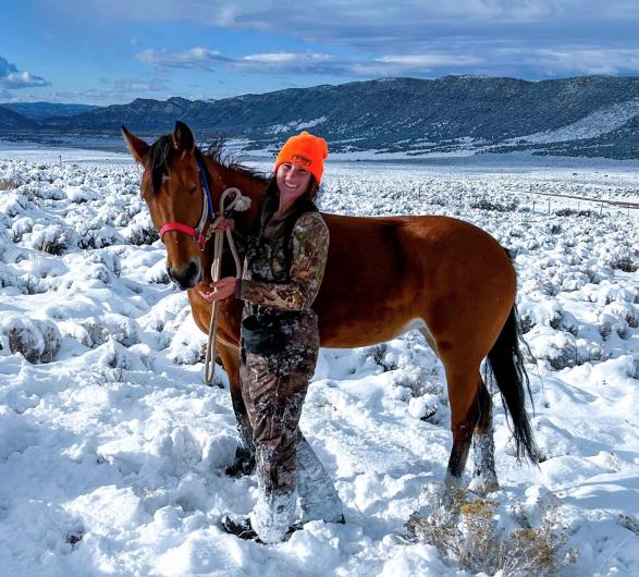 A horse in a snowy field with a hunter. 