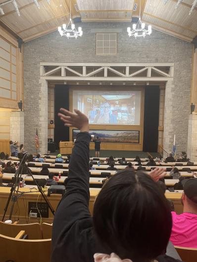 a group of people from the back watching a presentation. One person has their hand up in a wave.