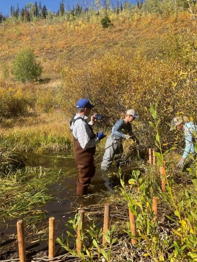 Three people with tools work to restore the normal path of the stream so it attaches to the wetlands.