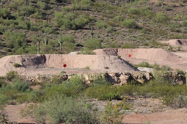 Red dots in front of a brown sediment barrier surrounded by green bushes and cacti. 