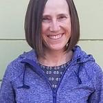 A woman wearing purple with short brown hair smiles at the camera. 