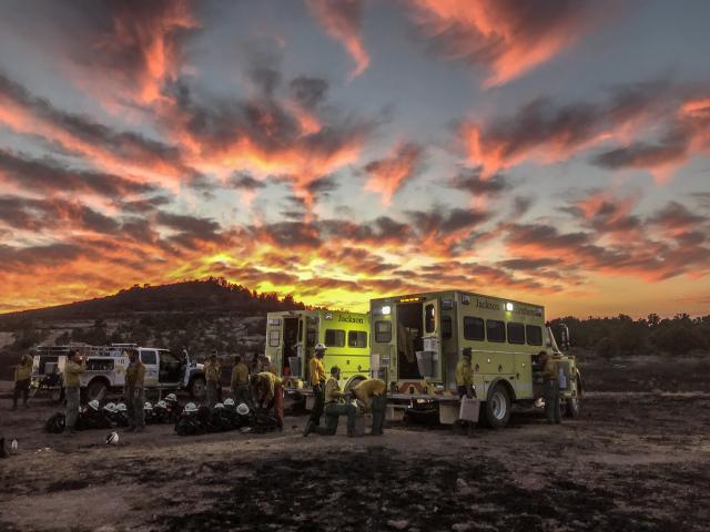 The sun sets behind two Jackson Hotshots trucks and crew.