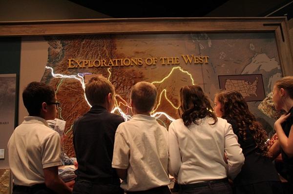 A group of children looking at an "Explorations of the West" map display at the Trails Center. 