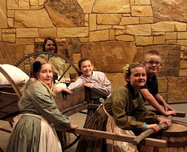 Five children dressed in period clothing in a wagon. 