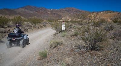 A four-wheeler on a  dusty desert road with a mountain in the background.
