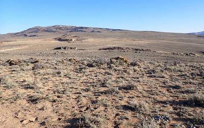 A desert landscape with a mountain and small mine in the background. 