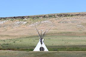 A Teepee stands in the middle of a field with a rising behind it. 