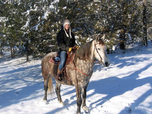 Woman rides horse in snow. 