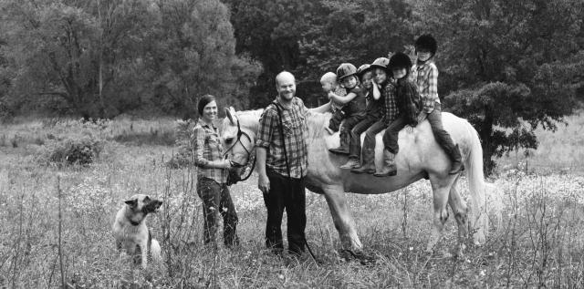 Family poses for picture with horse and dog in a field. 