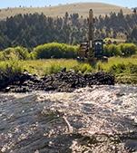 A wide creek flows in front of an excavator