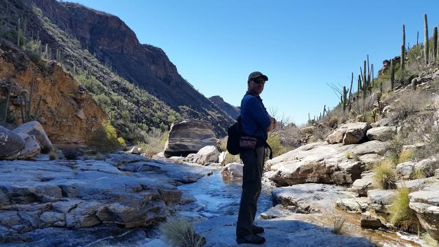 Man standing on a rock in a streambed with mountains to the side and in the background.