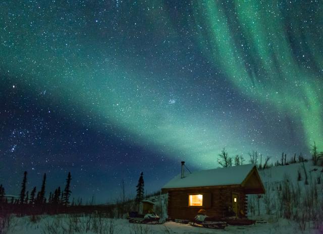 A cabin beneath a sky glowing with the Northern Lights.